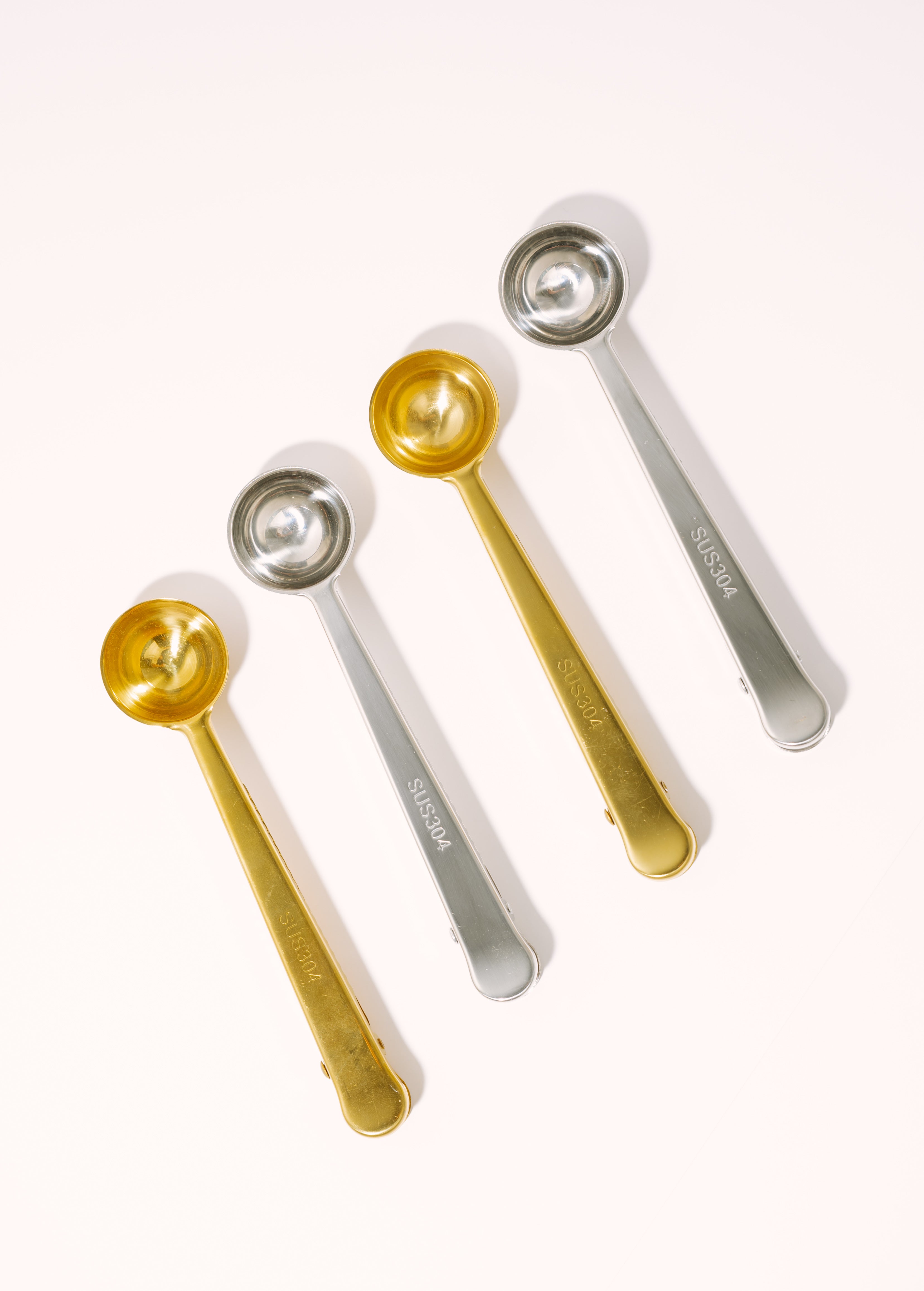 Set of five measuring spoons in gold and silver on a white background