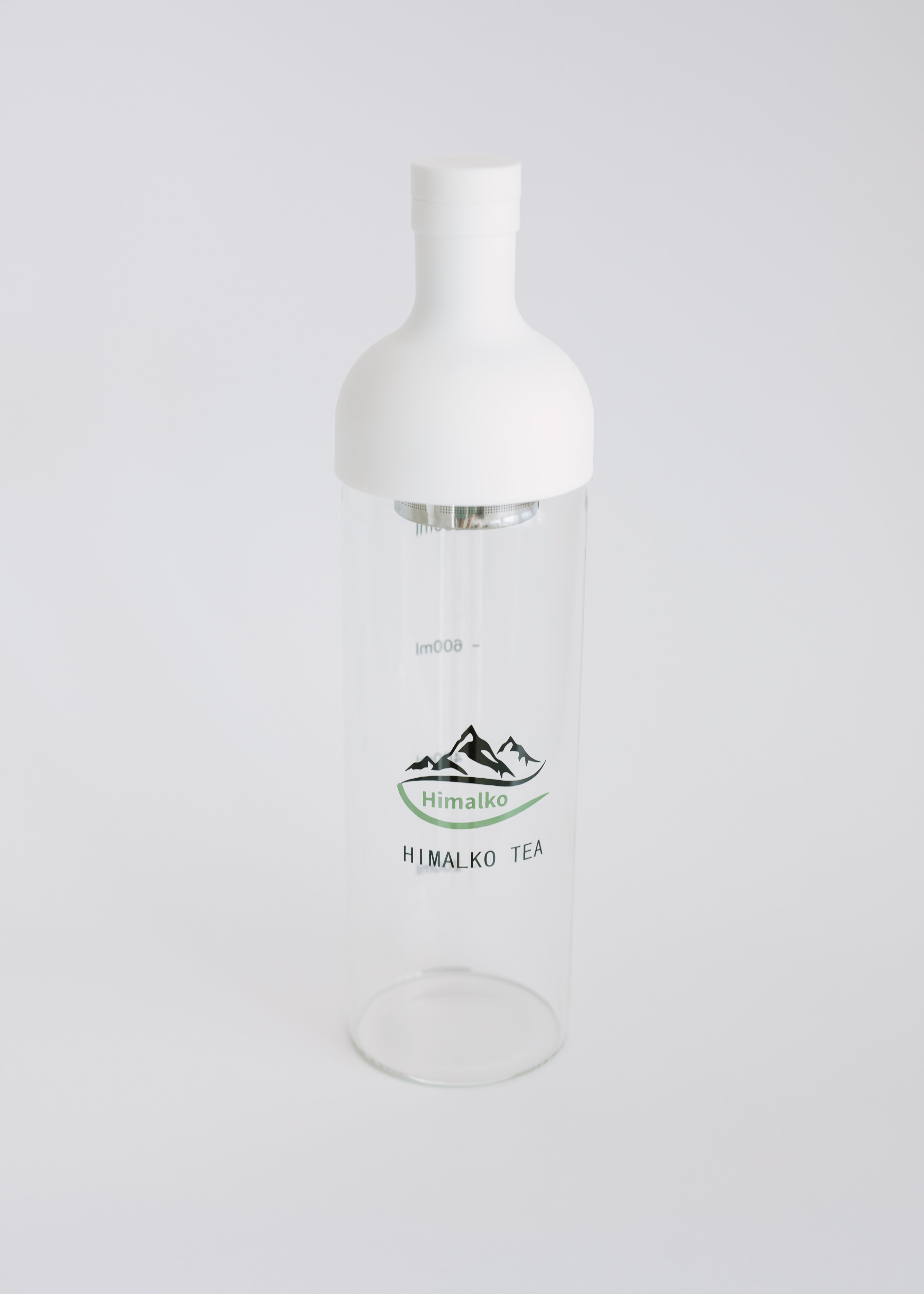 A clear glass bottle with a white plastic cap and a printed green and black logo reading 'Himalkó Tea' on the front, set against a plain light gray background.