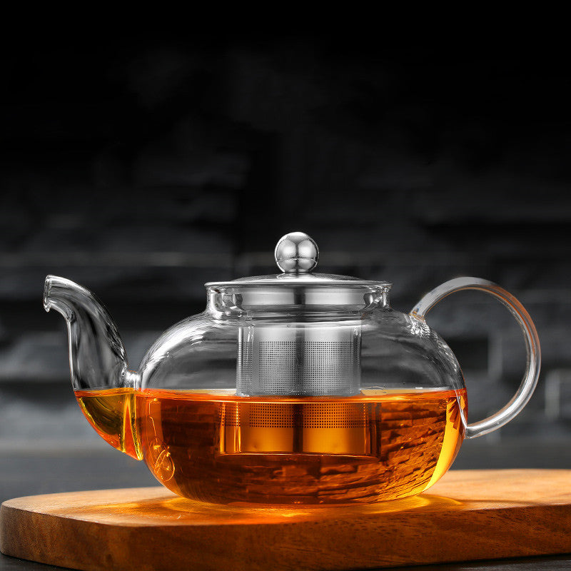 Clear glass teapot with tea on a wooden coaster against a dark background